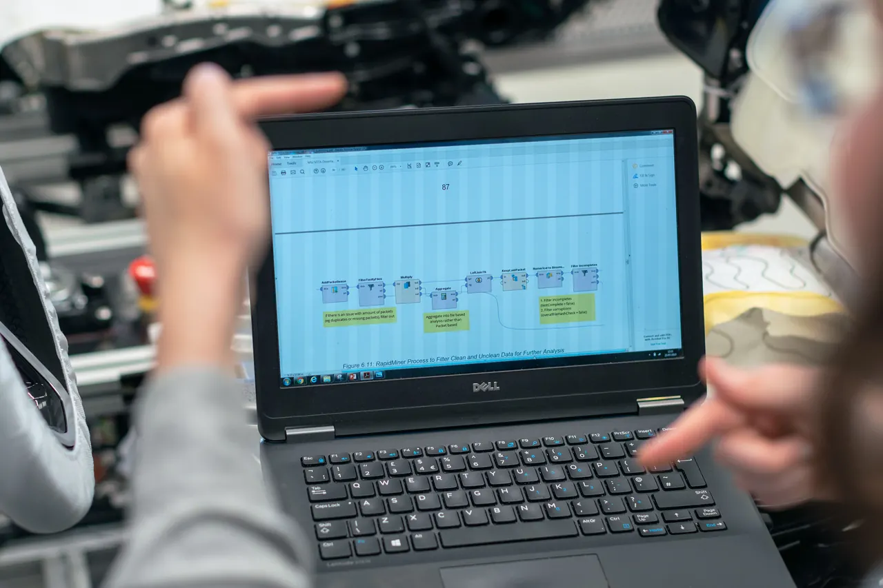 Personen betrachten Messdaten auf einem Laptop an einem technischen Arbeitsplatz.